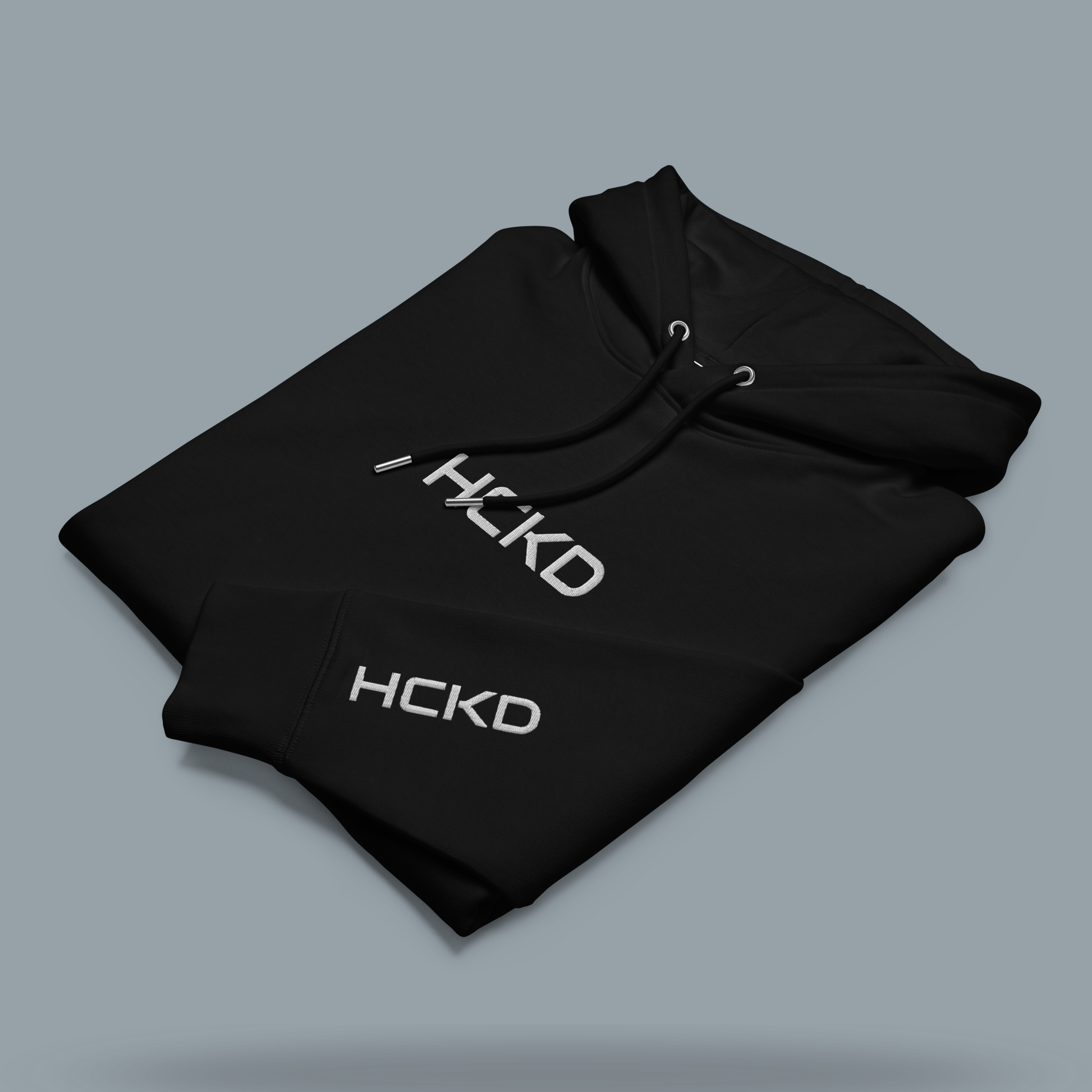 Black HCKD HOOD-01 hoodie laid flat, featuring modern design and metal-tipped drawcords for all-day comfort.