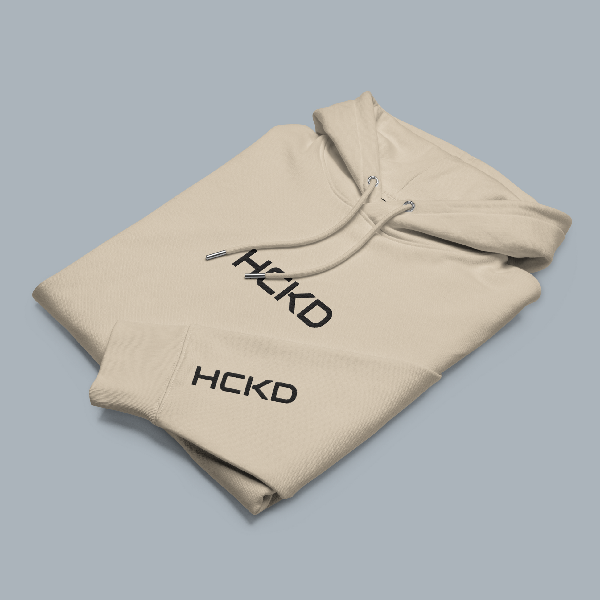 Cream HCKD hoodie showcasing modern design, featuring metal-tipped drawcords and kangaroo pocket for added comfort.